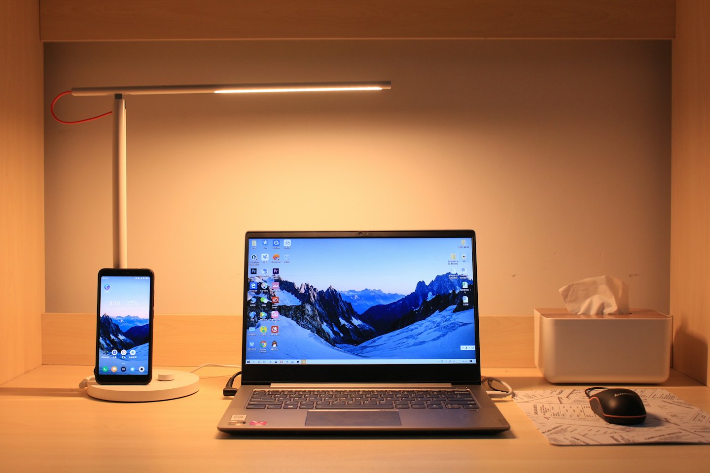 Laptop e smartphone in carica su una scrivania di legno.